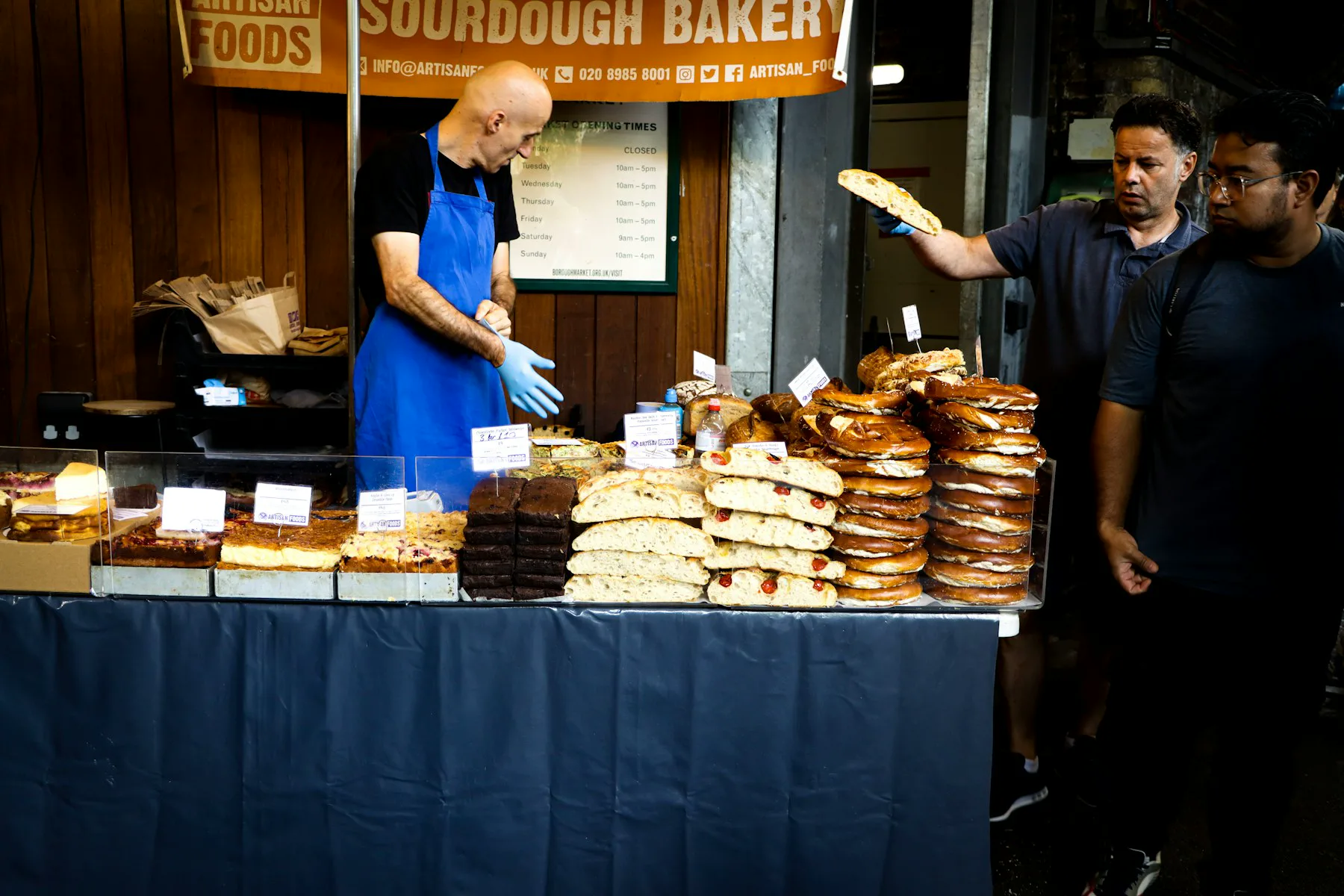 A baker serving customers at a market stall in London