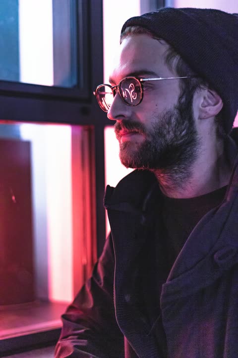 A man in glasses seen in profile beside a pink-lit window